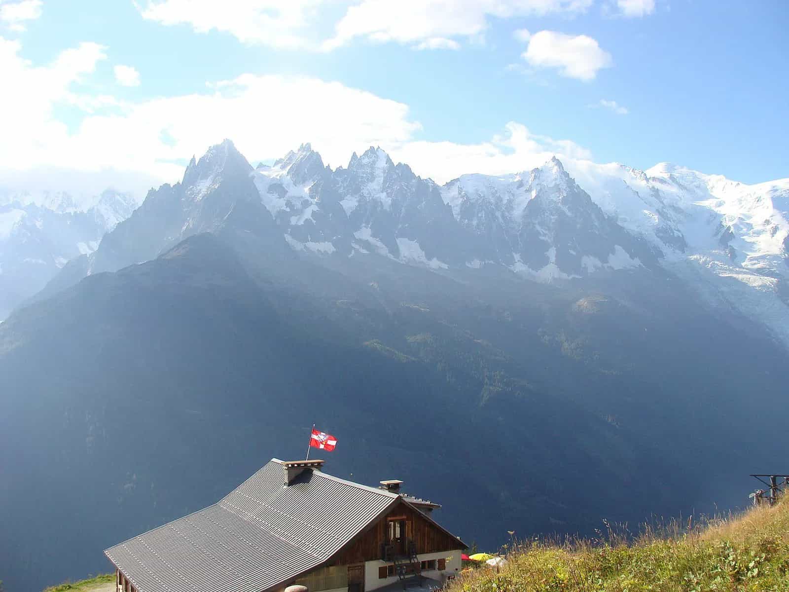 Alpine hut with Swiss flag below snow-capped mountains in the French Alps.
