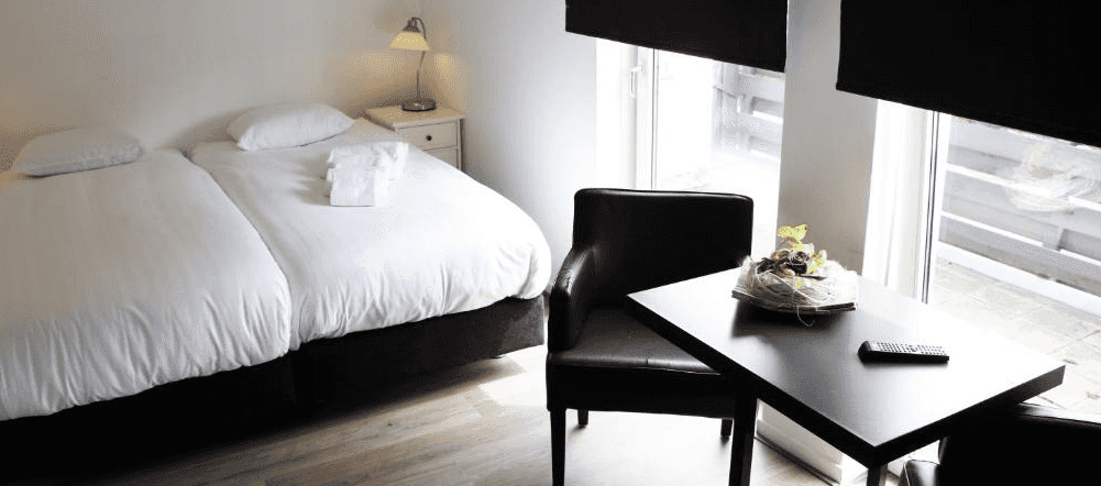 Twin beds with white linens, black table, leather chair, and bright window in a modern room.