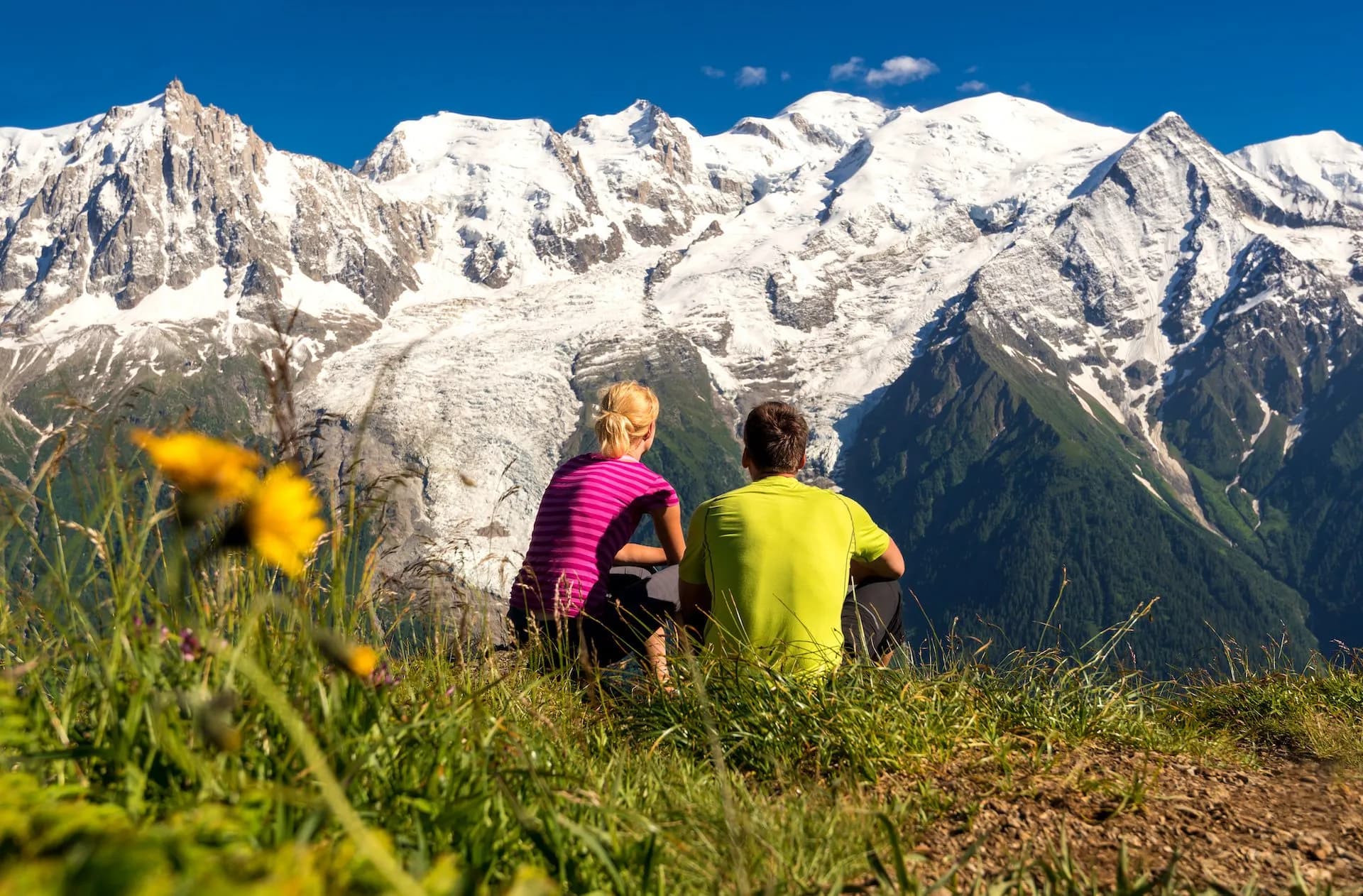 Hikers overlooking Mont Blanc glacier panorama from grassy viewpoint on sunny day
