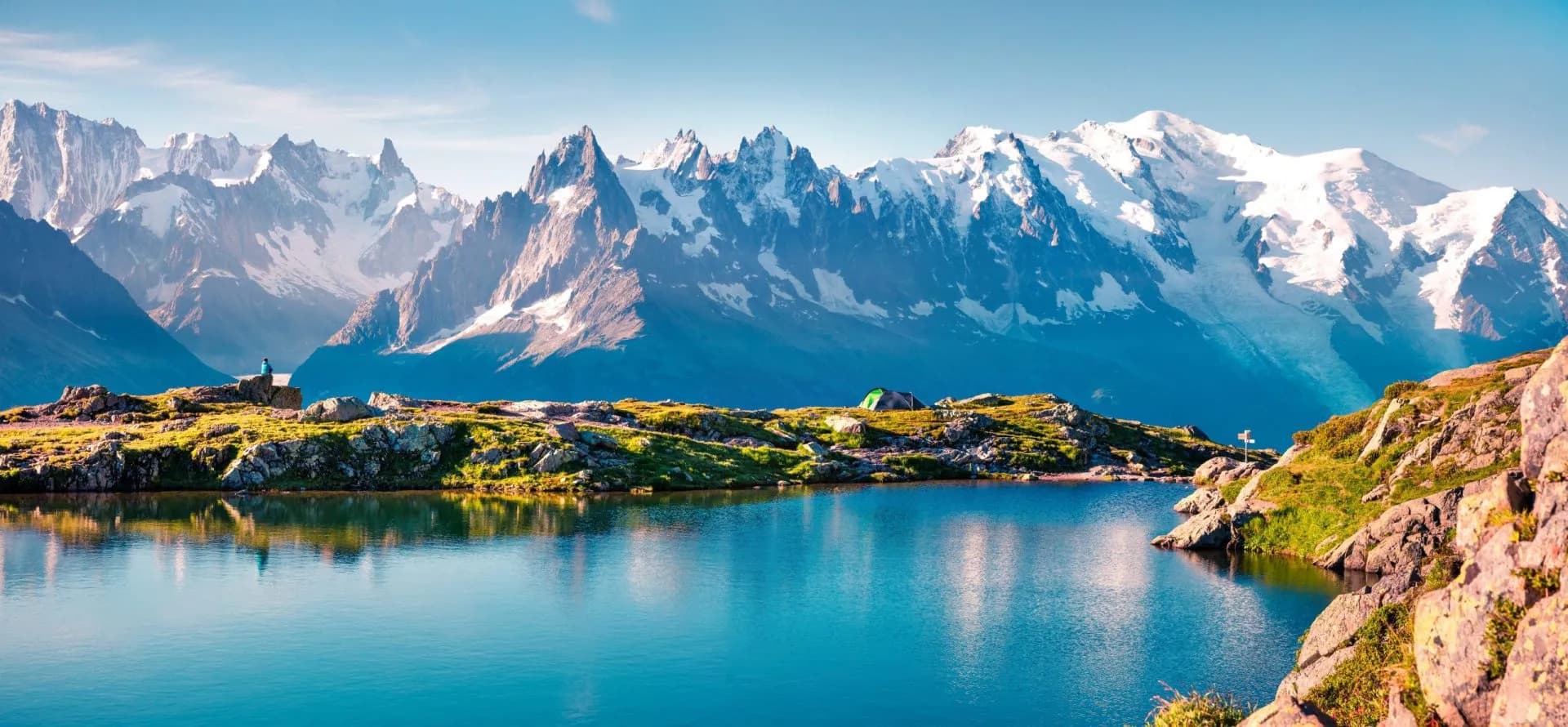 Alpine lake reflecting snow-capped Mont Blanc massif with camping on grassy shore