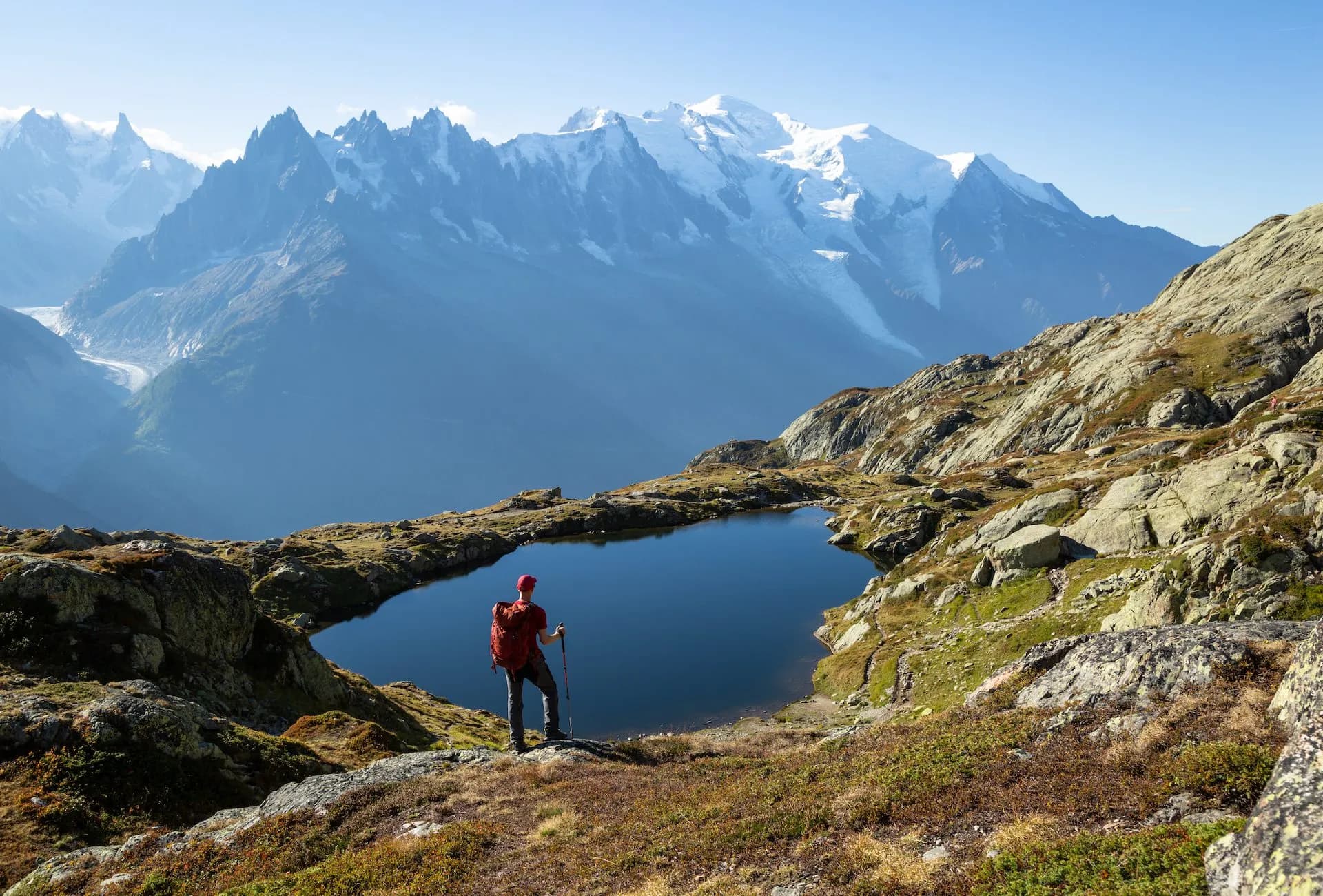 Hiker looking at Lac de Cheserys with snow-capped alpine mountains in the background.