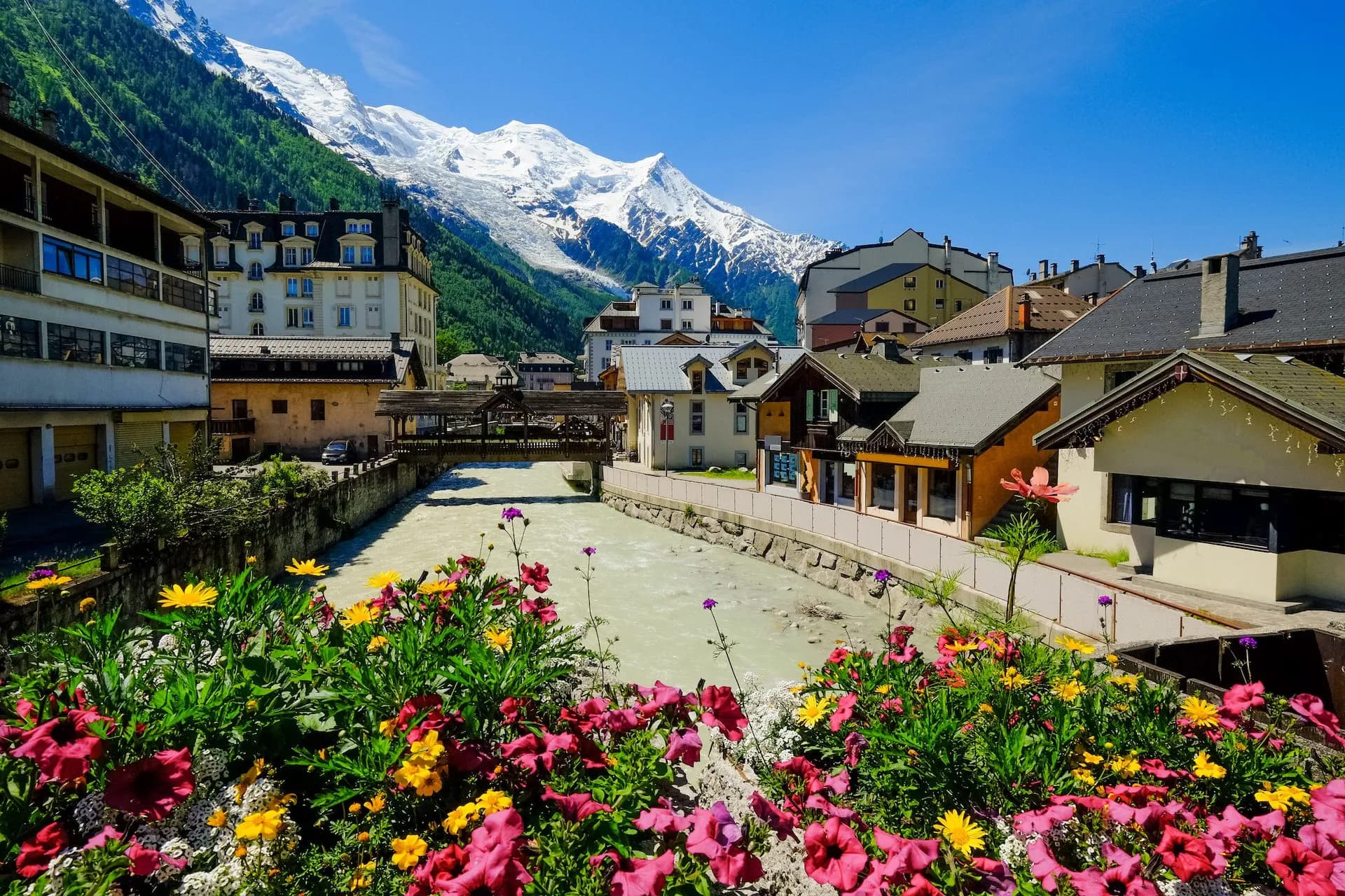 Chamonix downtown in summer with river, colorful flowers, and snow-capped mountains.