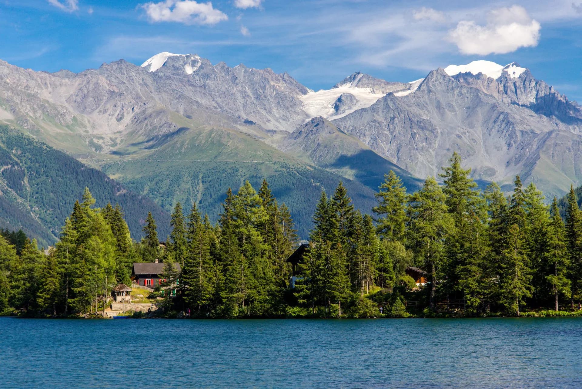 Alpine mountain lake Champex-Lac with snow-capped peaks, evergreen trees, and a lakeside cabin.