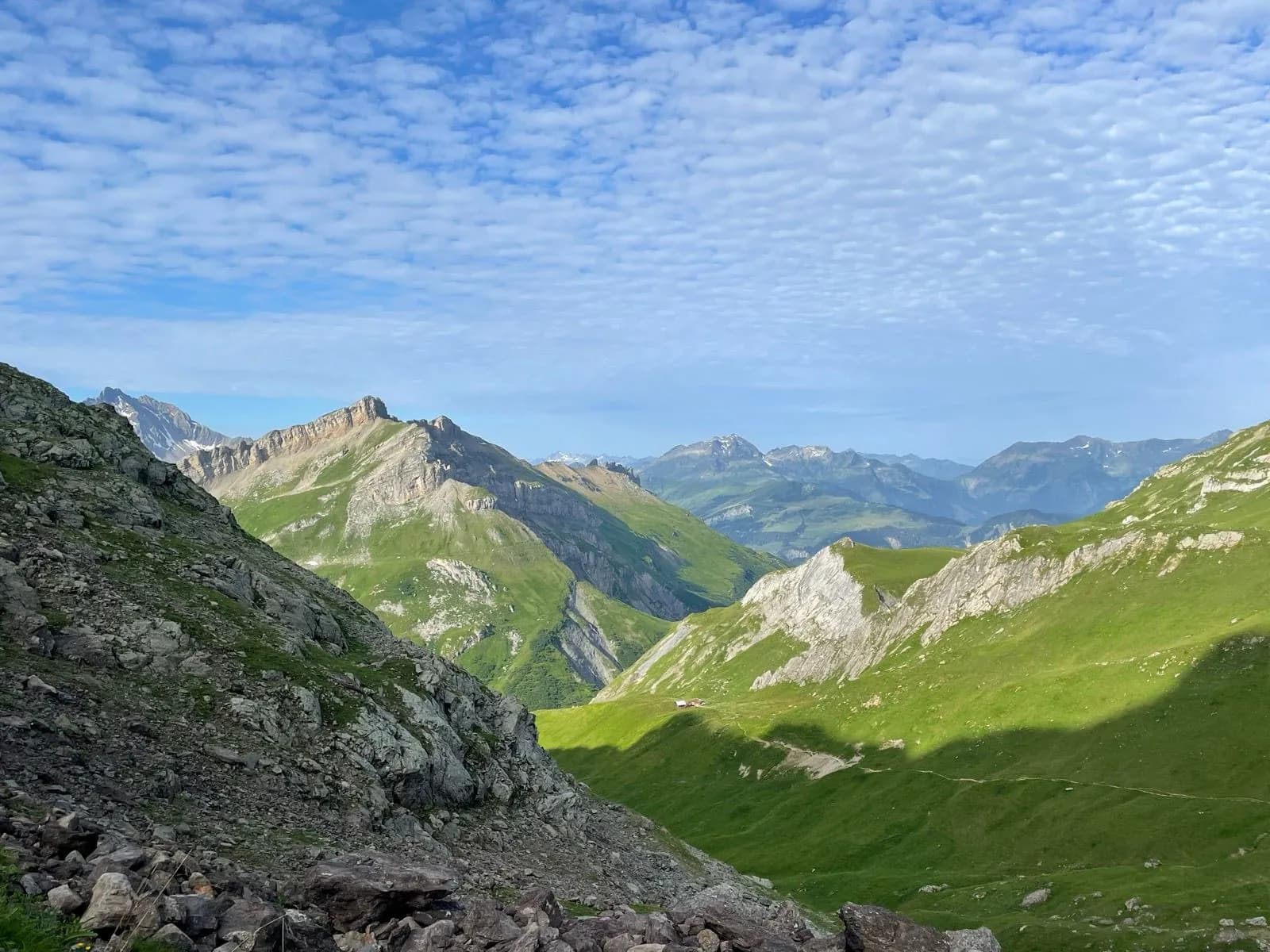 Mountain valley with green slopes, rocky foreground, and altocumulus clouds in blue sky