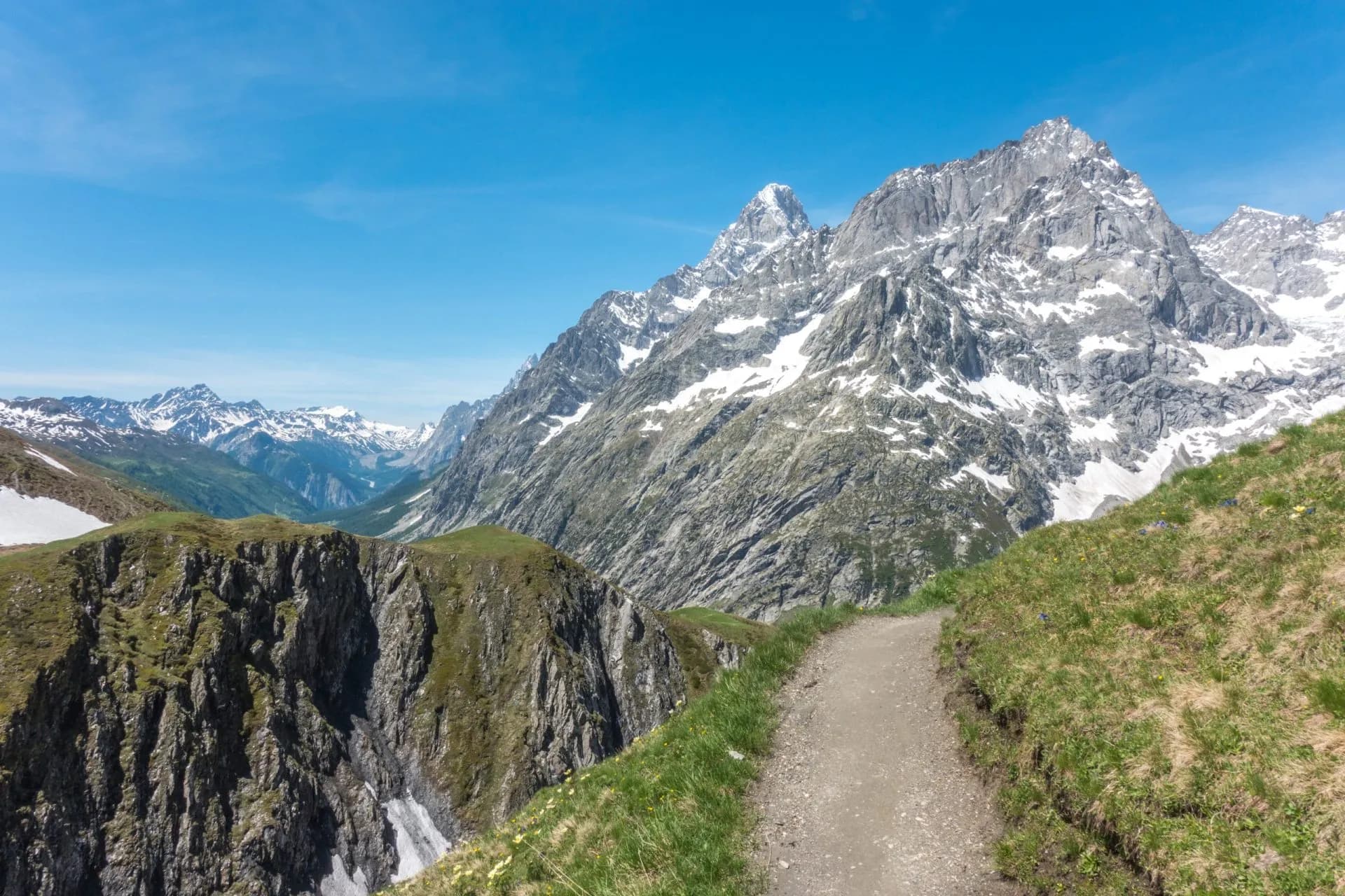 Hiking trail along a grassy ridge toward snow-capped mountains at Col du Ferret.