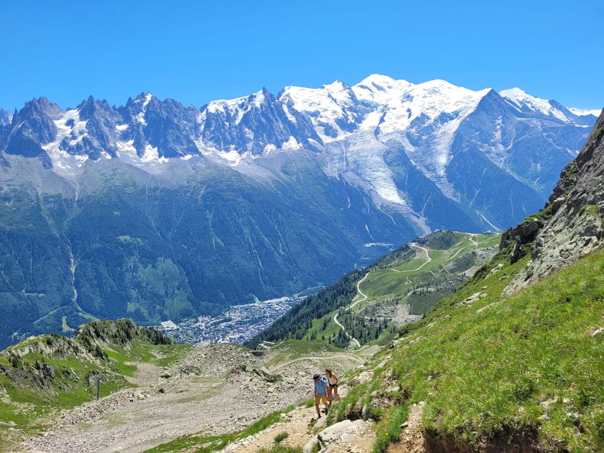 Hikers on trail overlooking Chamonix valley with snow-capped Brevent mountains