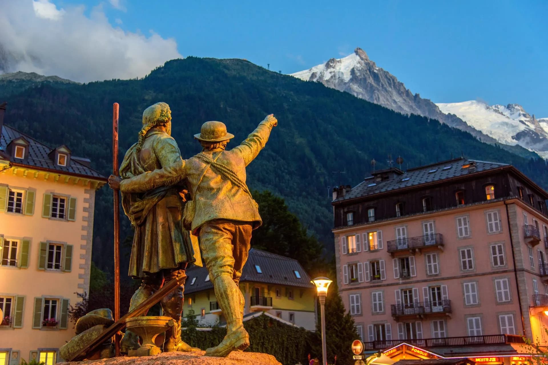 Monument to Alpinists in Chamonix with snowy mountains and illuminated buildings.