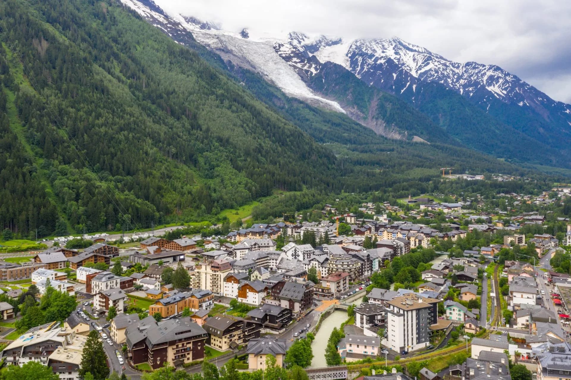 Aerial view of Chamonix town nestled in valley with forested slopes and snowy glacier mountains.