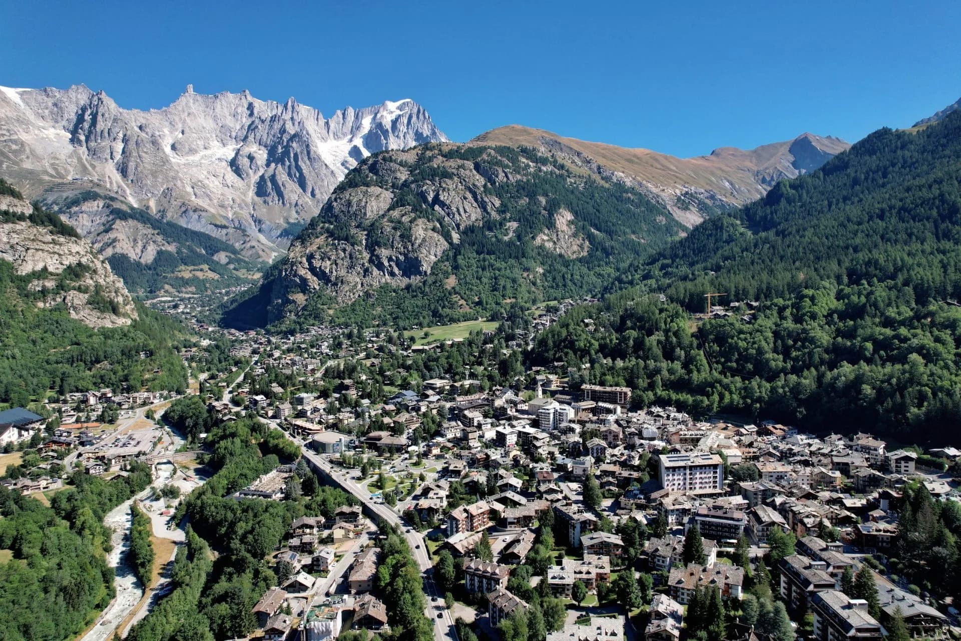 Aerial view of Courmayeur town nestled in a valley with rugged, snow-capped alpine mountains.