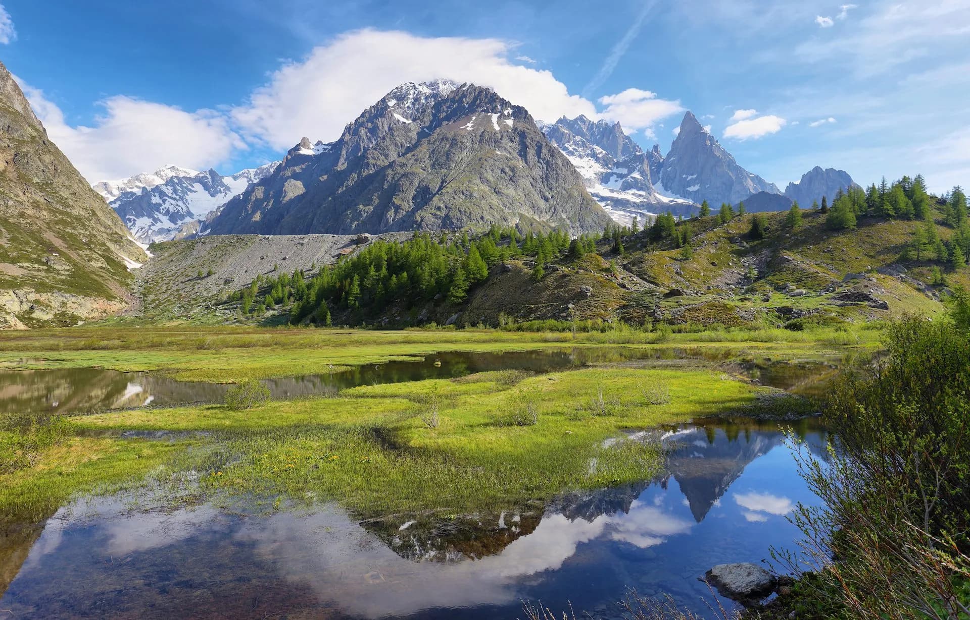 Snowy peaks of Aiguille Noire reflected in marshy water in Veny valley.