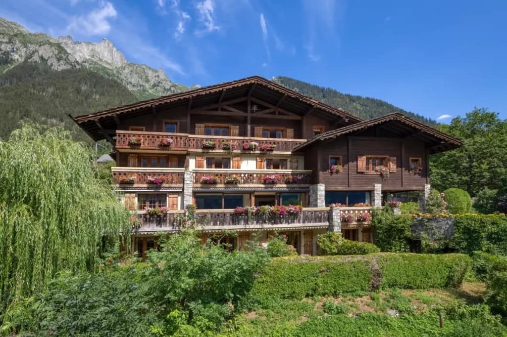 Chalet-Hotel du Bois with wooden balconies and flower boxes against a backdrop of green mountains.