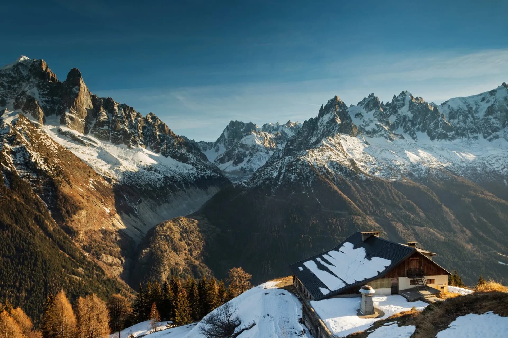 Mountain refuge hut with snow on the roof set against jagged, snow-capped peaks of Refuge de la Flégère.