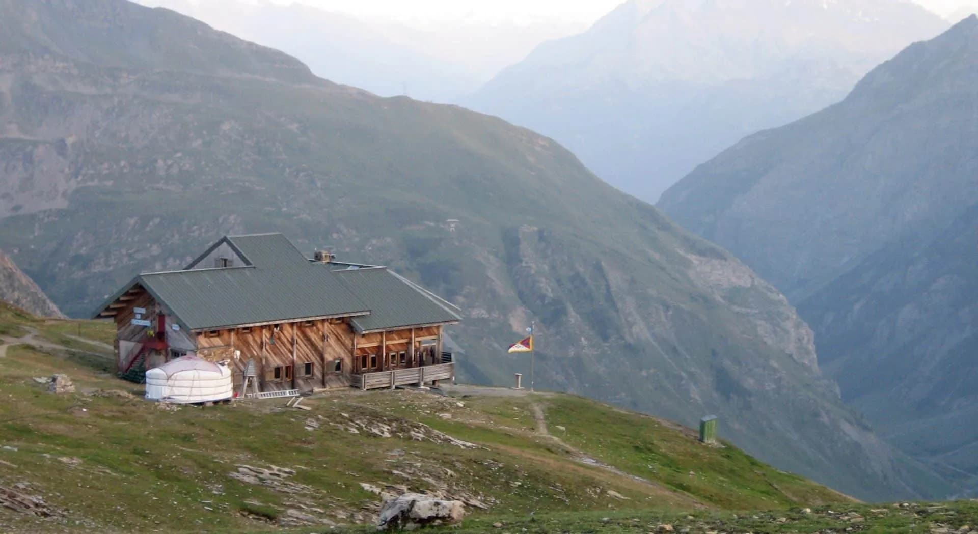 Refuge de la Croix du Bonhomme wooden mountain hut with yurt and flag against steep alpine valley.