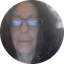 Close-up portrait of a woman wearing glasses with dark curly hair in a circular frame.