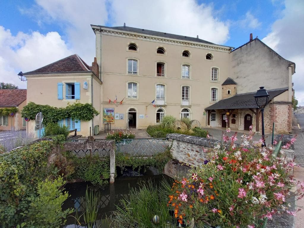 Historic building, possibly a former mill, with flowers and a small stream in Gite-le-Moulin.