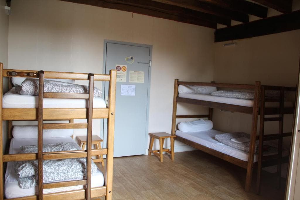 Two wooden bunk beds with white and patterned bedding inside a room with light walls and wooden beams.