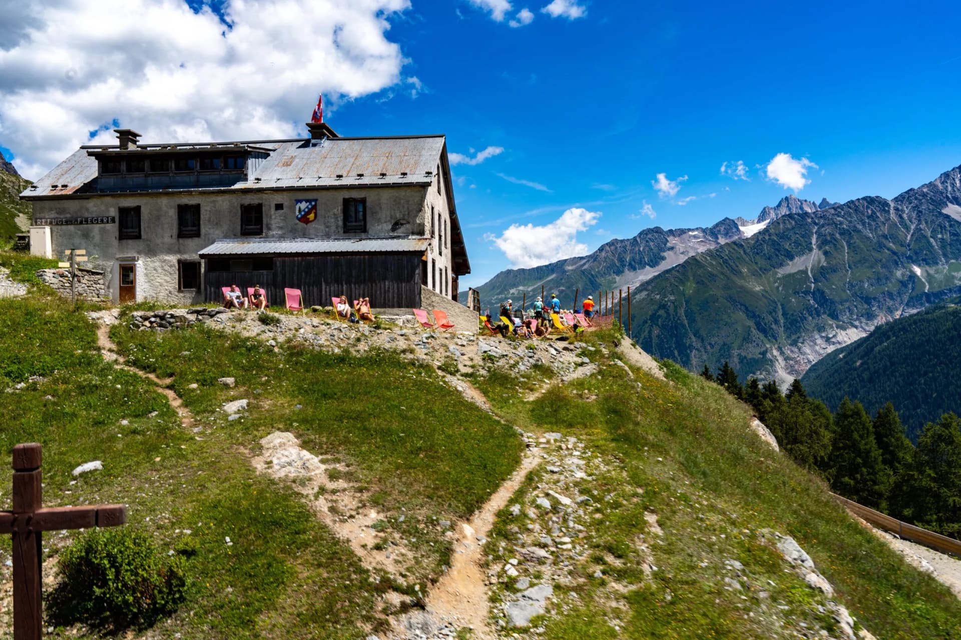 Refuge de la Flégère building with hikers resting on a grassy slope below rugged mountains.