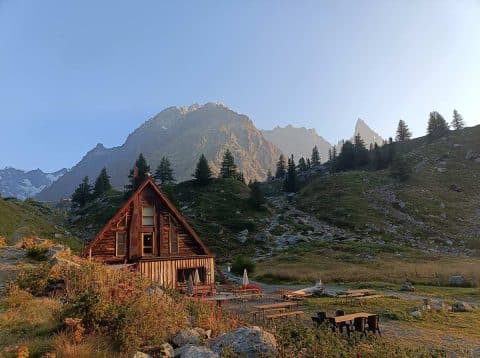 Wooden refuge du Combal cabin in a grassy alpine valley with tall mountains in the background.