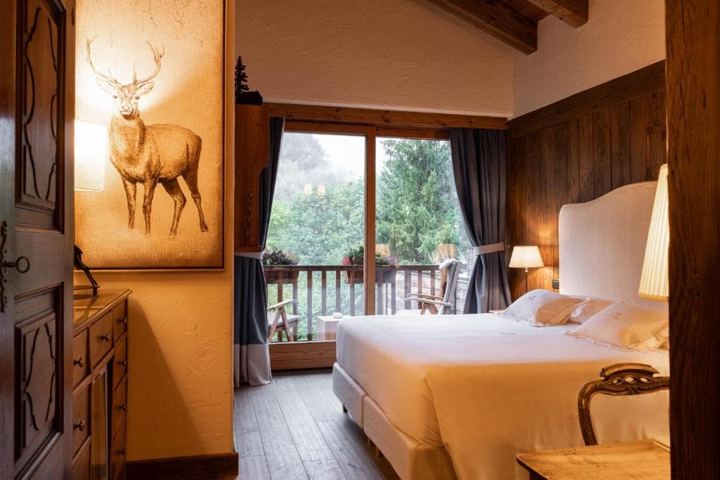 Cozy hotel bedroom with wood paneling, deer art, and balcony view of lush green forest.