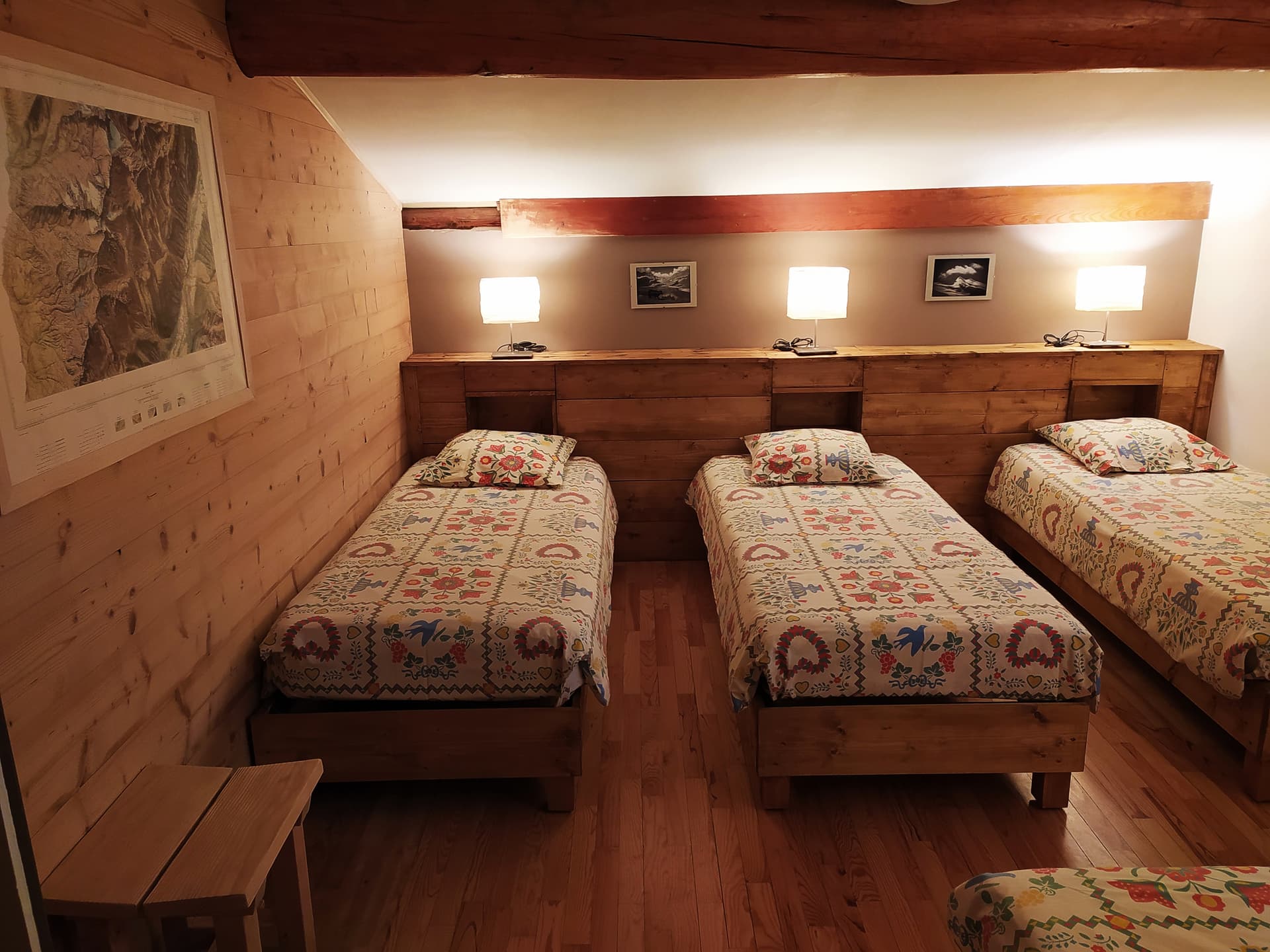 Three single beds with floral quilts in a wood-paneled room in Gite les Melezes.