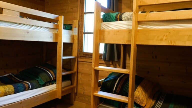 Wooden bunk beds with striped bedding inside a log cabin room near a window.