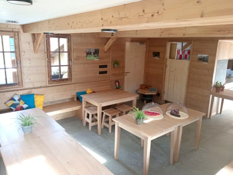 Wooden interior dining area with light wood tables, benches, and windows, likely a refuge.