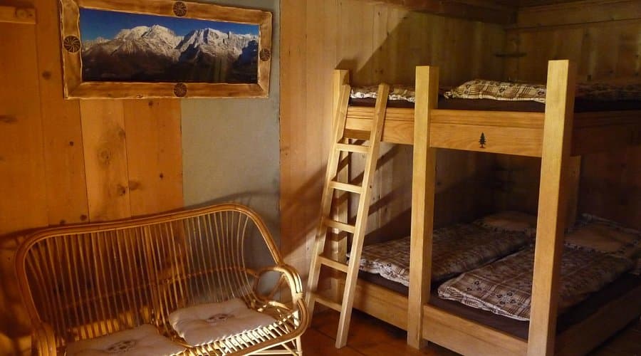 Wooden bunk beds and wicker sofa inside a rustic room at Refuge de Nant Borrant.