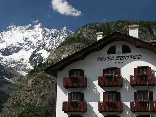 Hotel Berthod facade below snow-capped alpine mountains under blue sky