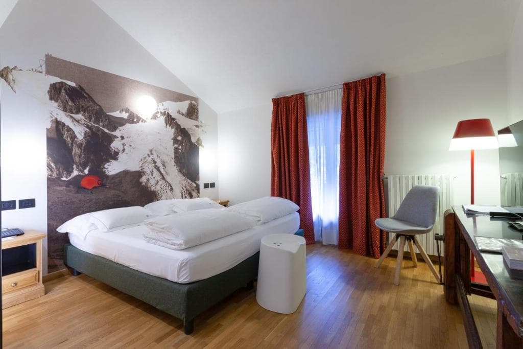 Hotel room with white bedding, wood floor, and large mountain mural wallpaper.