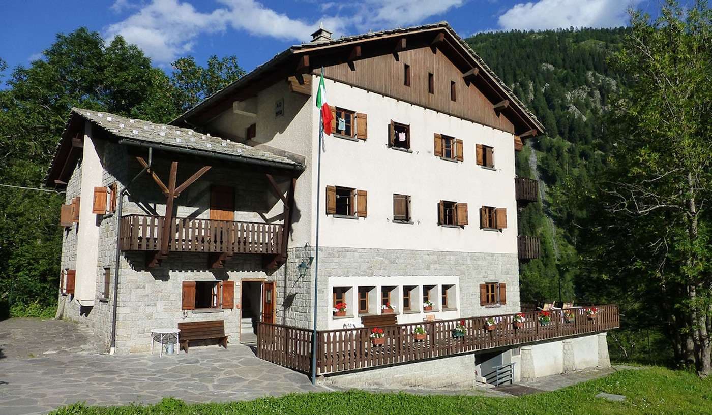 Rifugio Chapy mountain lodge with Italian flag, wooden balconies, and forested slope backdrop.