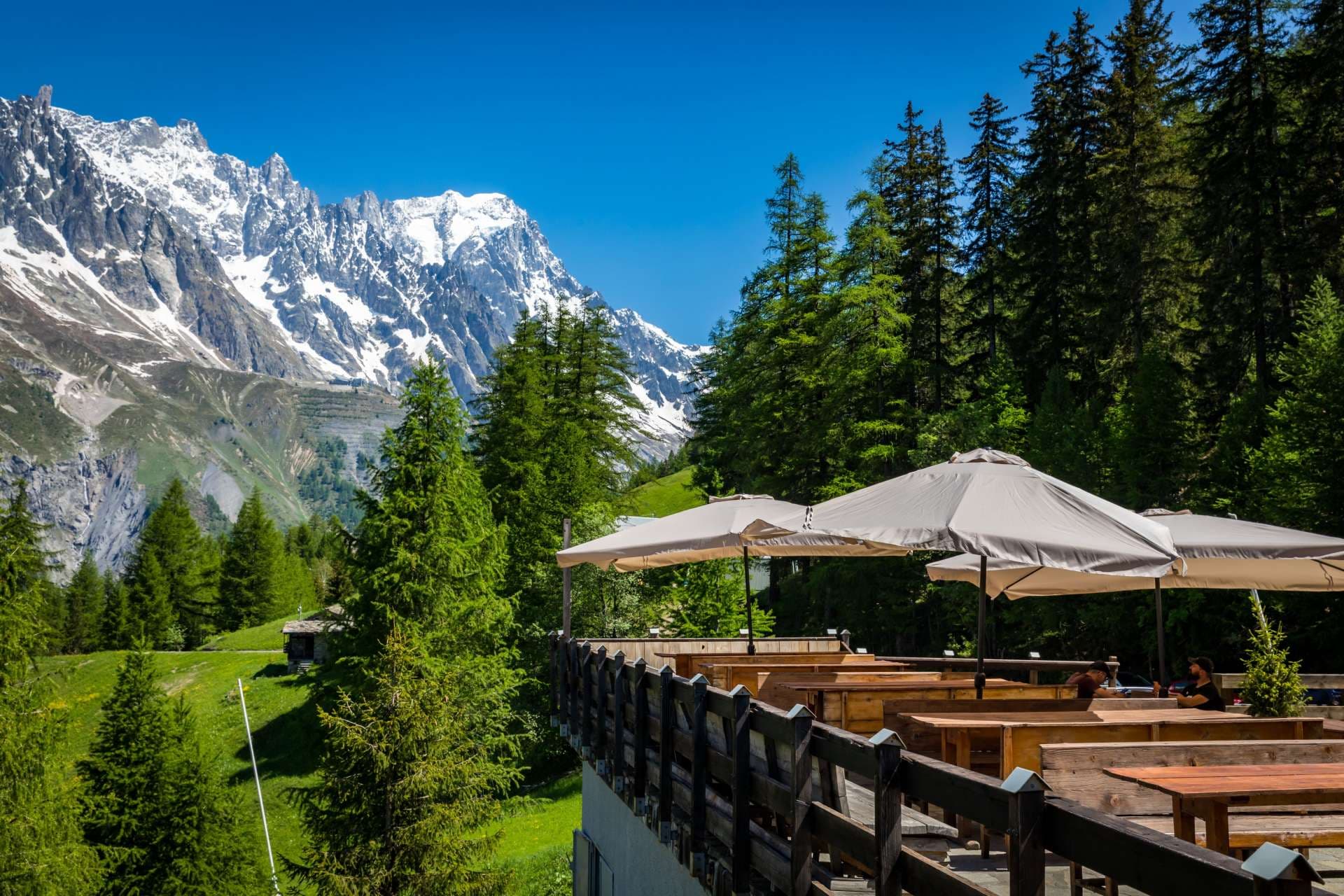 Outdoor terrace dining with snow-capped Monte Bianco mountains and pine forest backdrop