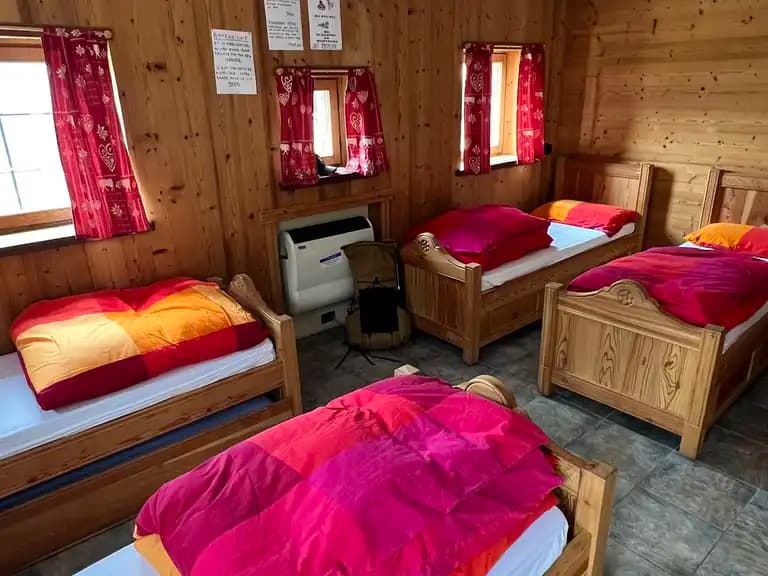 Wooden bunkhouse room with four beds, bright duvets, and red patterned curtains.