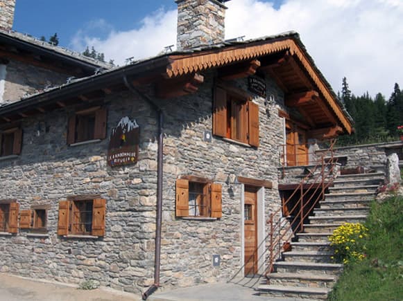 Stone refuge building with wooden shutters and exterior stairs in a mountainous setting