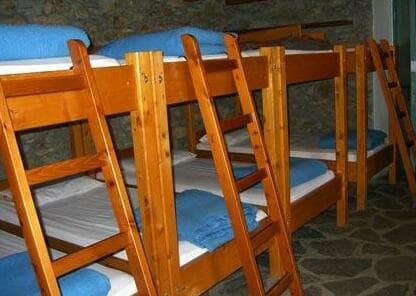 Wooden bunk beds with blue blankets inside a stone-walled Rifugio Maison Vieille.