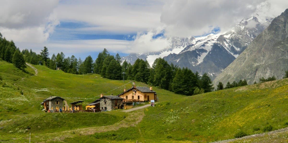 Rifugio Maison Vieille mountain refuge on green hillside below snow-capped peaks.