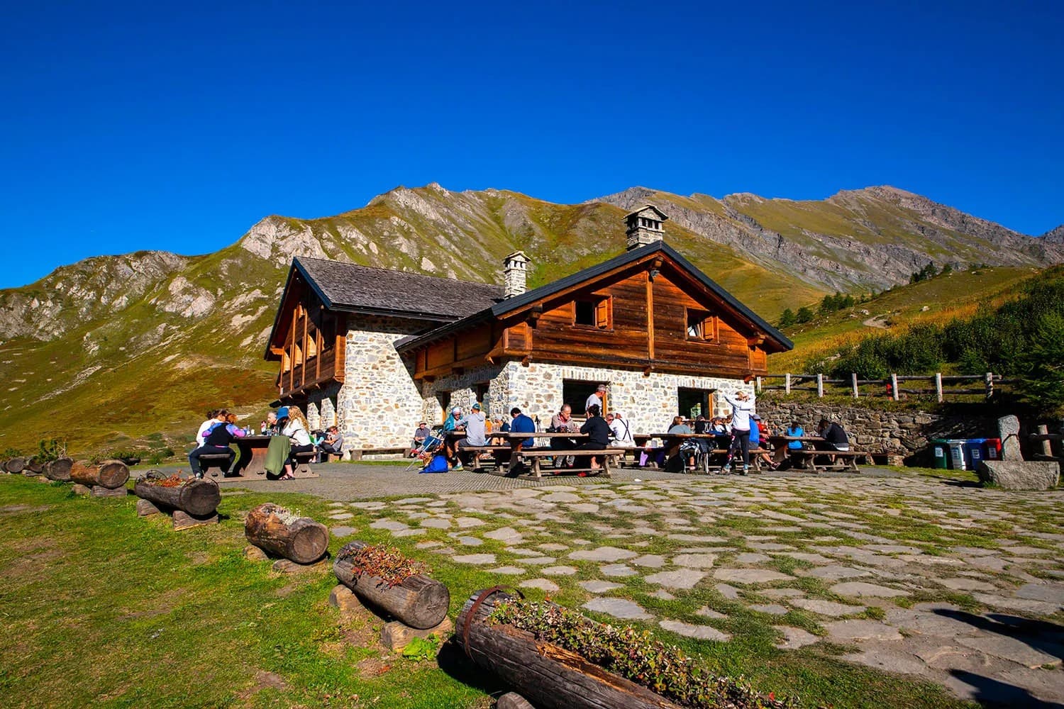 Rifugio Walter Bonatti mountain hut with hikers resting outdoors against large green mountains.