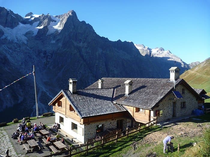 Rifugio Walter Bonatti stone mountain hut with hikers dining outdoors below snowy peaks.