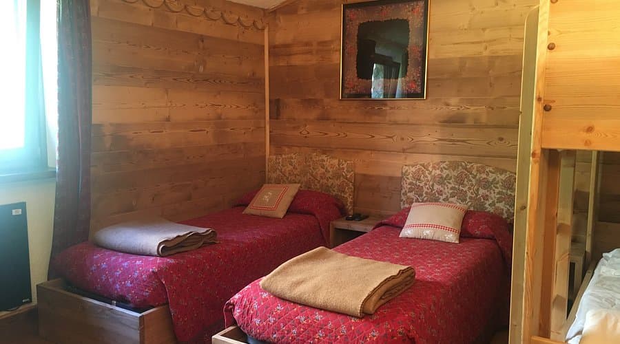 Twin beds with red quilts and wood paneling inside Chalet Val Ferret.