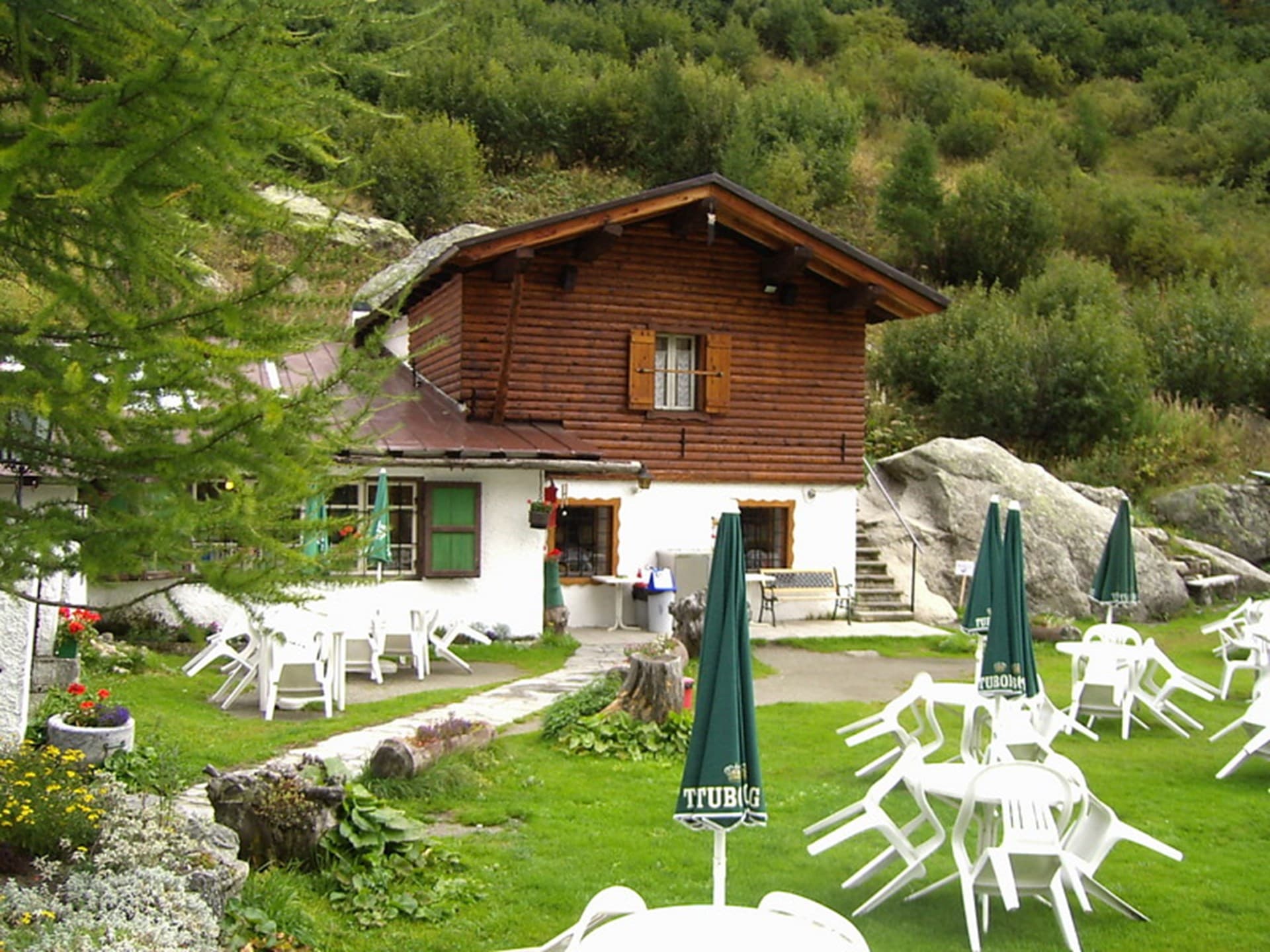 Chalet Val Ferret with stacked white chairs and closed green umbrellas on grassy area.