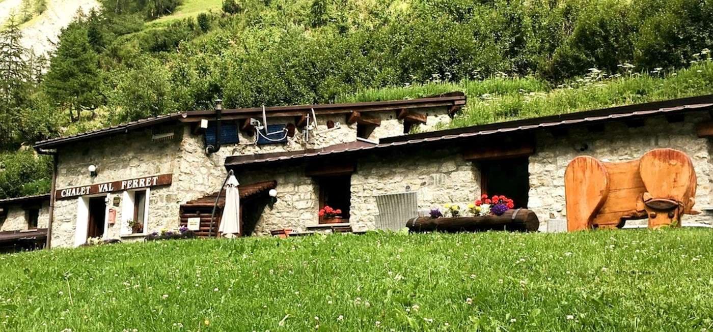 Chalet Val Ferret stone building in grassy alpine setting with wooden cow sculpture