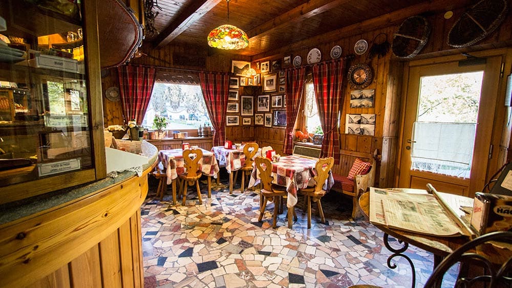 Cozy wooden restaurant interior with checkered tablecloths and mosaic floor at Hotel Lavachey.