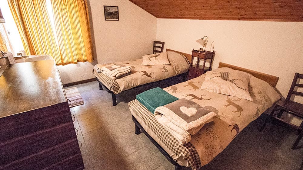 Twin beds with deer-patterned bedding in an attic room with wood ceiling and orange curtains.