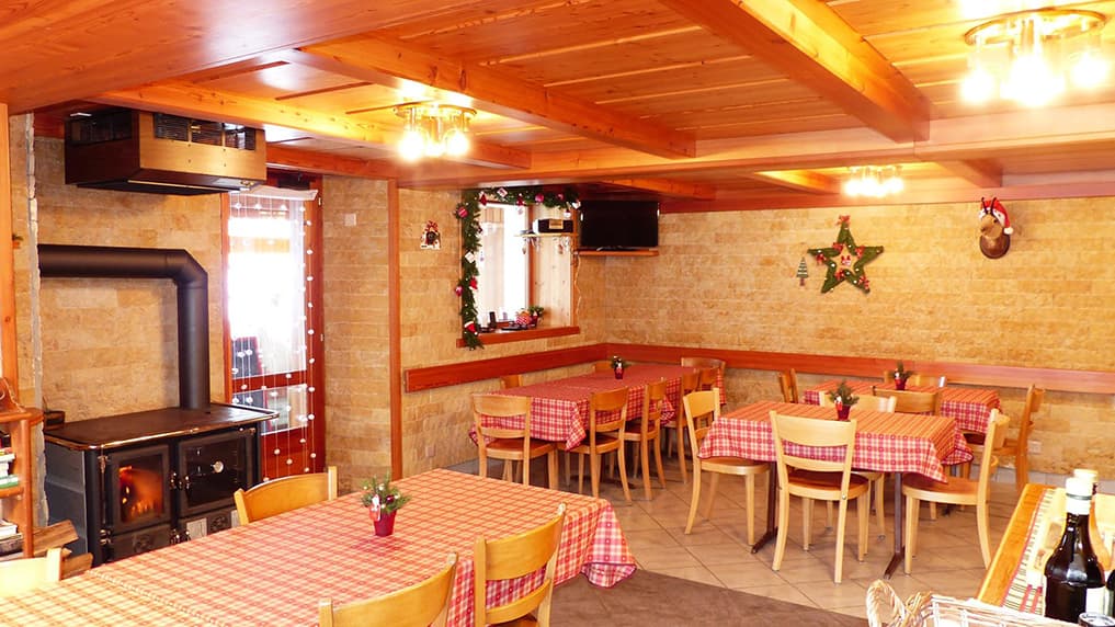 Cozy dining room with wood ceiling, stone walls, wood stove, and Christmas decor at Hotel du Col de Fenêtre.