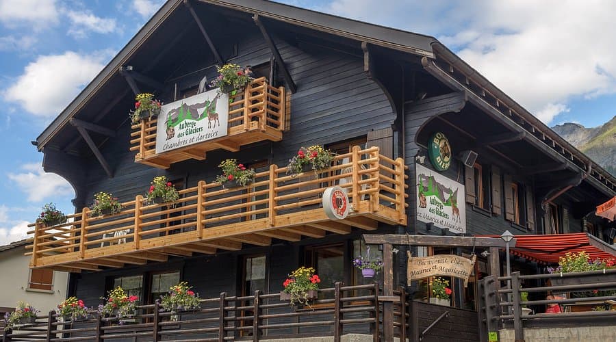 Auberge des Glaciers chalet with wooden balconies and flower boxes under a blue sky.