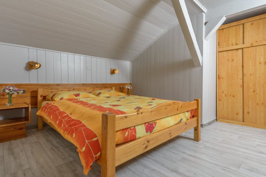 Attic bedroom with wooden bed, orange butterfly bedding, and pine wardrobe at Auberge des Glaciers.