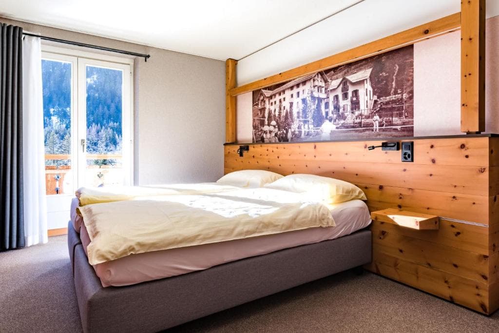Hotel room with wooden headboard, bright bedding, and balcony view of snowy forest.