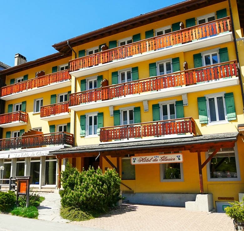 Hotel du Glacier building with yellow facade, wooden balconies, and green shutters under blue sky.