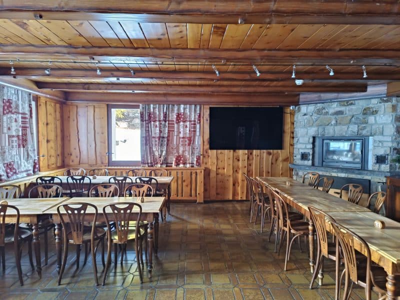 Rustic dining room with wood paneling, long tables, chairs, and stone fireplace at Relais d'Arpette.