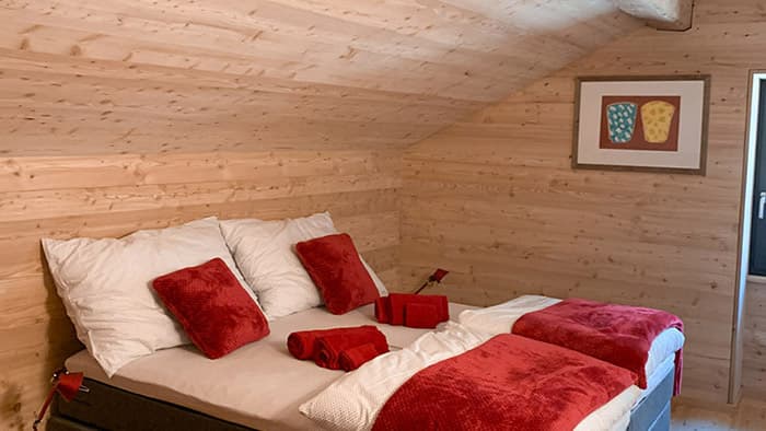 Bedroom with wood paneling, double bed with white and red linens, and framed art.