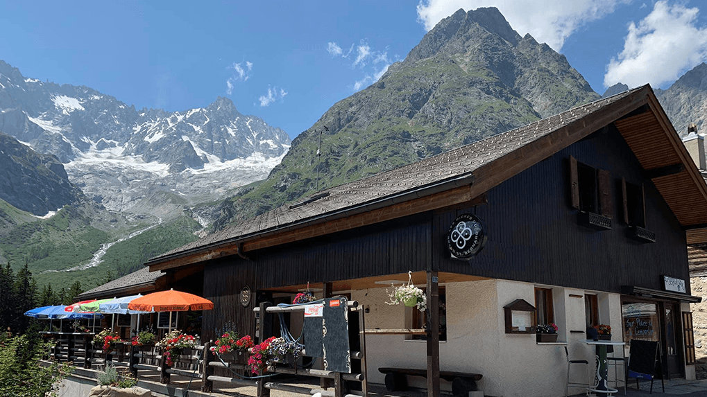 Gîte de la Fouly restaurant terrace with flower boxes against massive snow-capped alpine mountains.